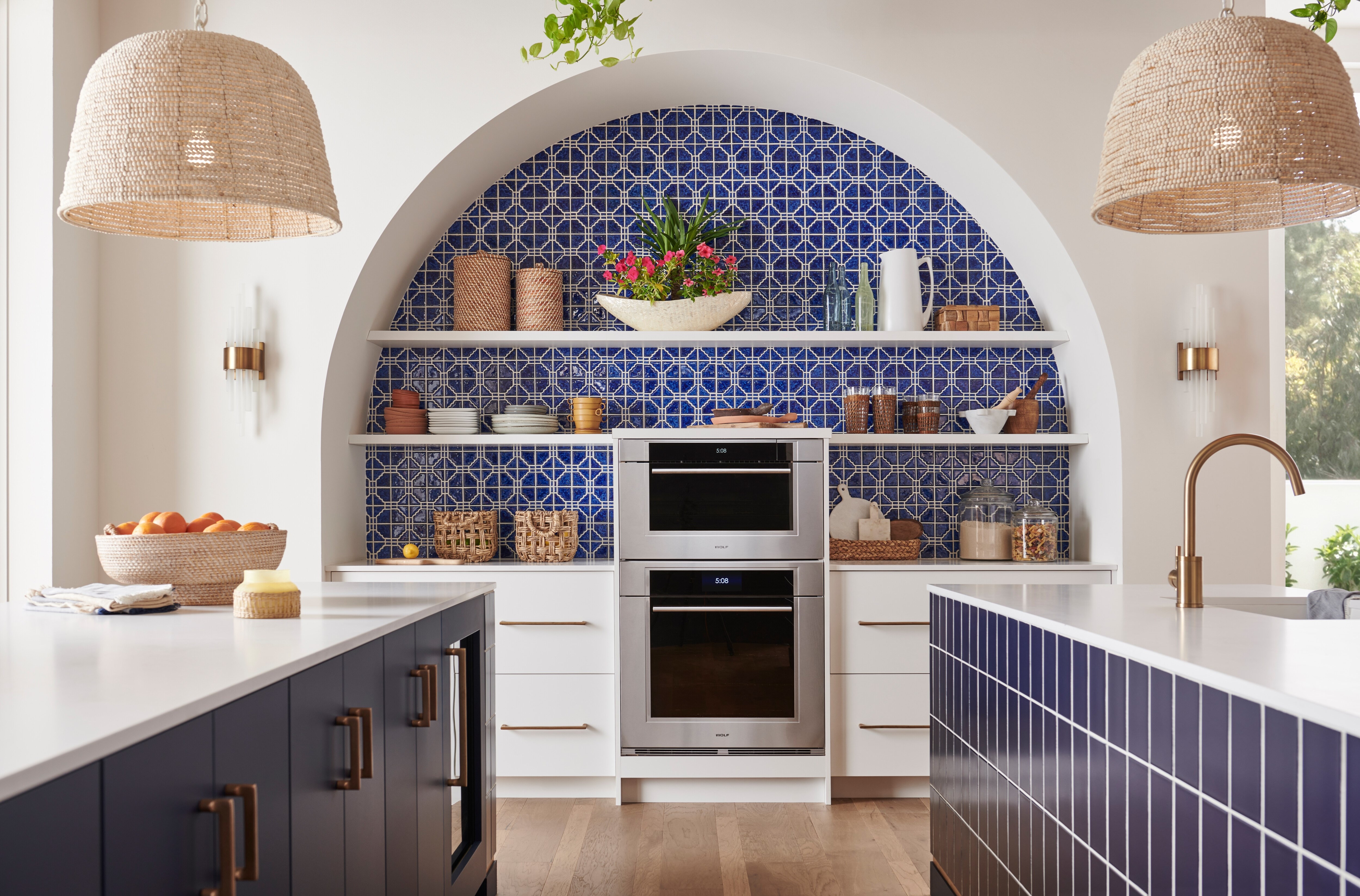 Wolf 30 inch M Series Transitional Convection Steam Oven and Wolf 30 inch M Series Transitional Built-In Single Oven shown together in a custom Mediterranean kitchen design featuring blue tiles, open sheles and gold fixtures